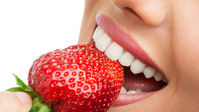 Woman with perfect teeth about to bite into a strawberry