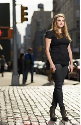 Dr. Yungelson poses in all black and high heels on a brick road, unknown Manhattan street in background.